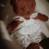 A cuddly brown teddy bear sits comfortably on a soft chair, dressed in heart-patterned clothes.