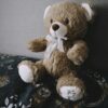 photo by lisa from pexels A soft brown teddy bear with a bow sits on a bed with a floral-patterned blanket, creating an inviting and warm atmosphere.