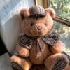 Adorable teddy bear in plaid sitting by a sunlit window, perfect for decor or children's themes.