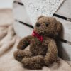 Charming teddy bear with a red bowtie, resting against a rustic wooden crate on a soft, cozy blanket.