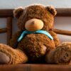 Cute brown teddy bear with blue scarf seated on wooden bench, perfect for cuddling.